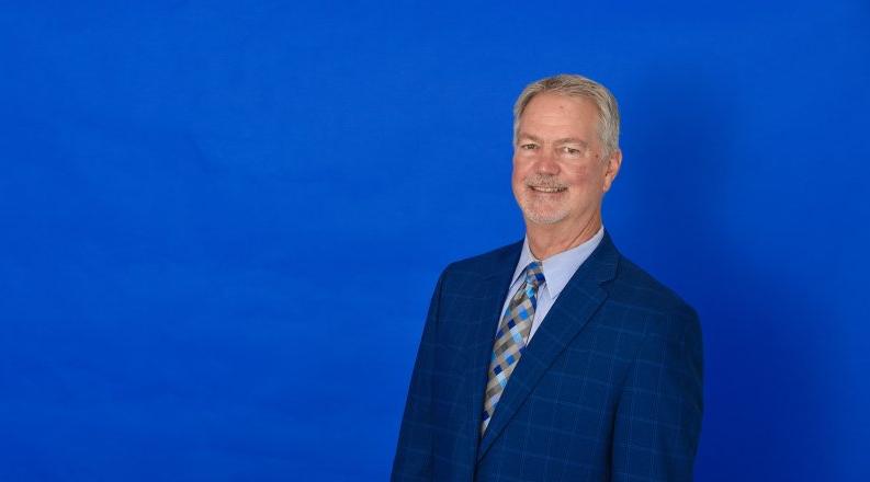 Horizontal headshot of a man against a blue background.