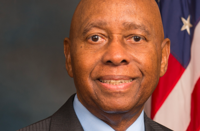 A Black male is posed in front of the American flag. 